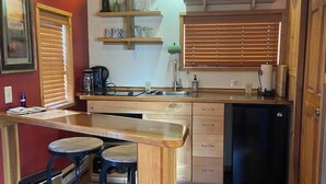 A compact kitchen with wooden cabinets, a black refrigerator, and a small bar area with stools.