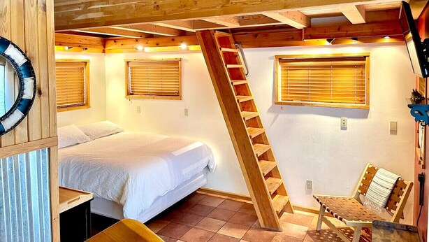 A bedroom with a bunk bed, a wooden ladder, and a chair.