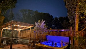 A hot tub with a wooden deck and a covered seating area with string lights.