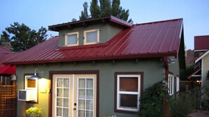 A two-story house with a red metal roof, a front door with glass panels, and a small porch area with potted plants.