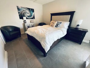 A bedroom with a bed, a nightstand, a chair, a painting, and a Wi-Fi sign.