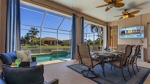 Amplia habitación con un gran ventanal con vistas a una piscina, un comedor con mesa y sillas, y ventiladores de techo.