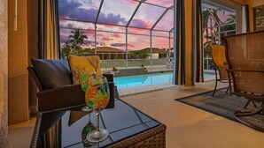 Un balcón con muebles de mimbre, una mesa de vidrio y vista a una piscina y palmeras.