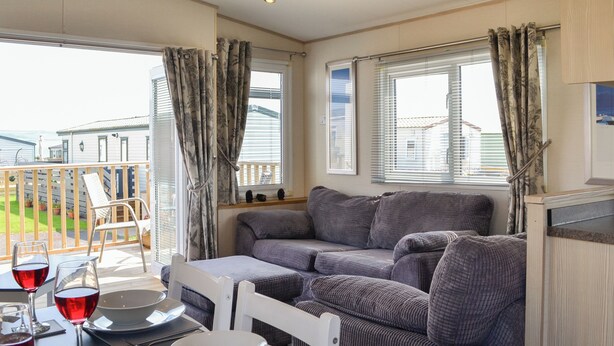 Un espacio de sala cómodo con un sofá, una mesa de comedor lista para dos personas y un balcón con vistas a casas.