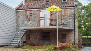 A two-story stone building with a balcony, a staircase, and a yellow umbrella. - 1 bedroom accommodation in Wells (Wells)