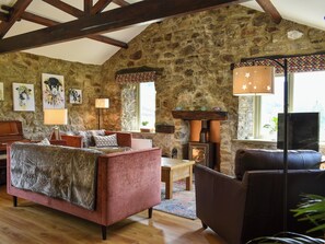 A rustic room with stone walls, wooden beams, a fireplace, and a cozy seating area with a sofa and armchair.