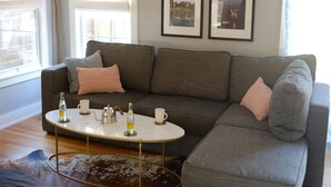 A living room with a grey sofa, a coffee table, and two framed pictures on the wall. - Cozy Multi-Property Bungalow in Central Austin - Cowboy pool (Austin)