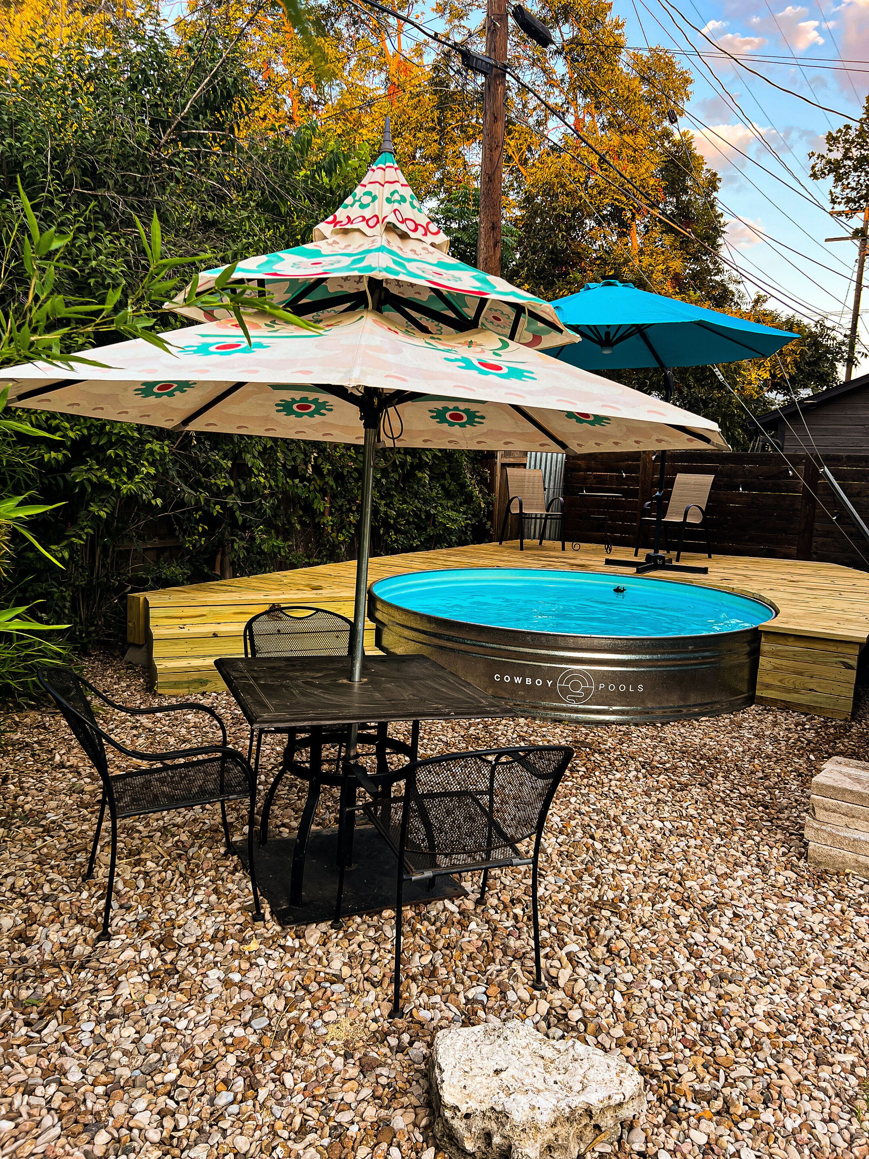 Ein Außenpoolbereich mit Whirlpool, umgeben von einer Holzterrasse, mit Metallstühlen und -tischen bestückt.