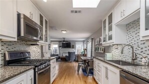 A modern kitchen with white cabinets, a granite countertop, stainless steel appliances, and a dining area with a table and chairs. - Cozy Multi-Property Bungalow in Central Austin - Cowboy pool (Austin)