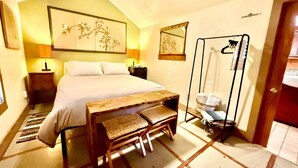 Une chambre à coucher comprenant un lit, des tables de chevet, un banc en bois, un miroir et un ventilateur de plafond.