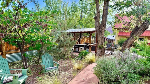 Un espace patio avec des fauteuils Adirondack verts, un barbecue couvert et une terrasse en bois.
