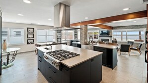 Une cuisine moderne dotée d’un îlot central, d’appareils électroménagers intégrés et d’une grande fenêtre donnant sur l’océan.