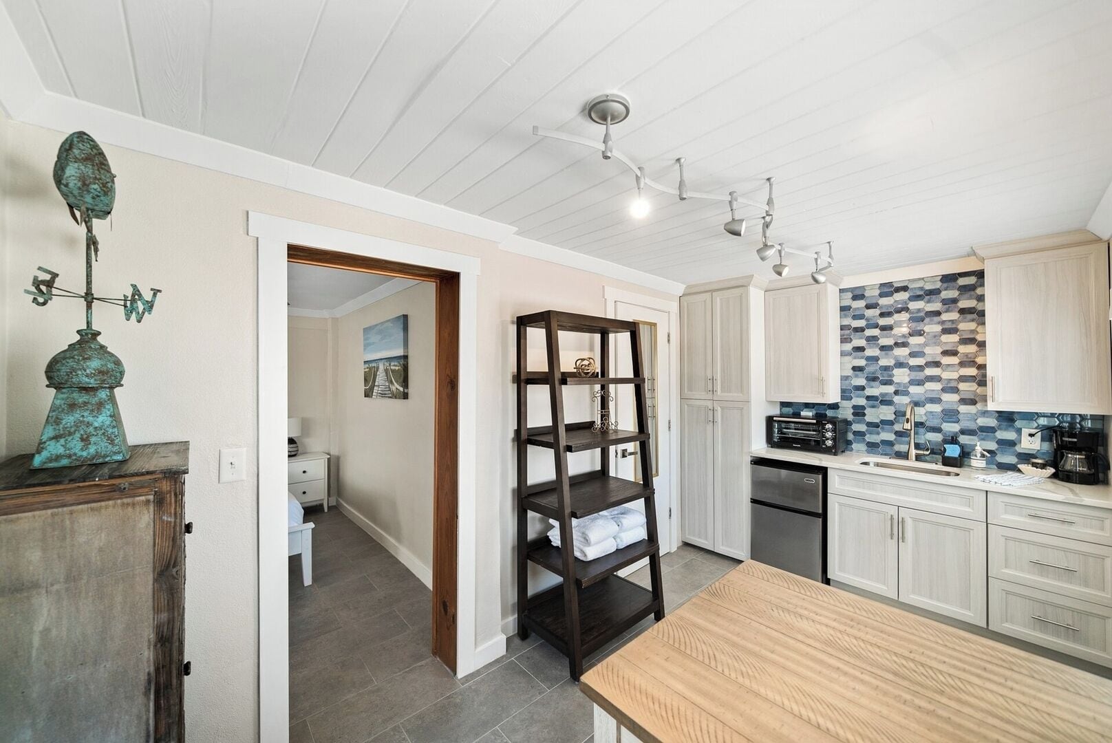 A modern kitchen with white cabinets, a wooden table, and a blue-tiled backsplash.