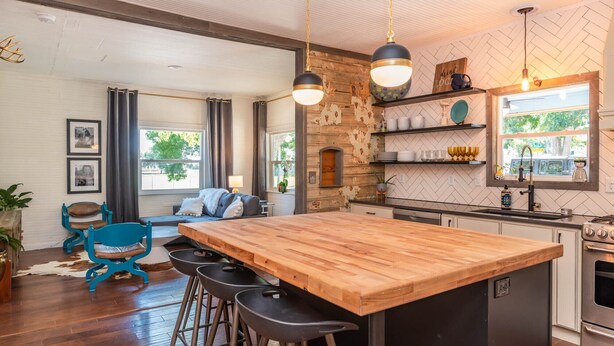 Een moderne keuken met een houten kookeiland, barstoelen en een accentmuur van steen.