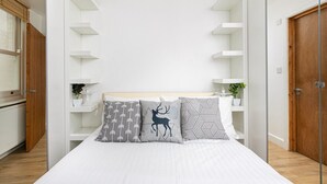 A modern bedroom with a bed, white walls, and built-in shelving.
