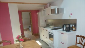 A compact kitchen with white cabinets, a stove, and a coffee maker. There is a dining table with chairs and a vase with flowers.
