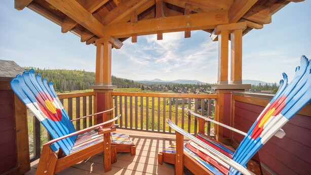 A wooden deck with two Adirondack chairs and a view of a forested landscape. - Hot Tub | Winter Getaway & Mountain Views (Fraser)