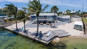 A waterfront property with a dock, palm trees, and a large house with a covered patio area. - Compass 2BR Suite - Gourmet Kitchen - Water view (Cocoa Beach)