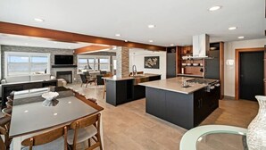 A modern kitchen with a central island, a dining area with a glass table, and a view of the ocean through large windows. - Compass 2BR Suite - Gourmet Kitchen - Water view (Cocoa Beach)