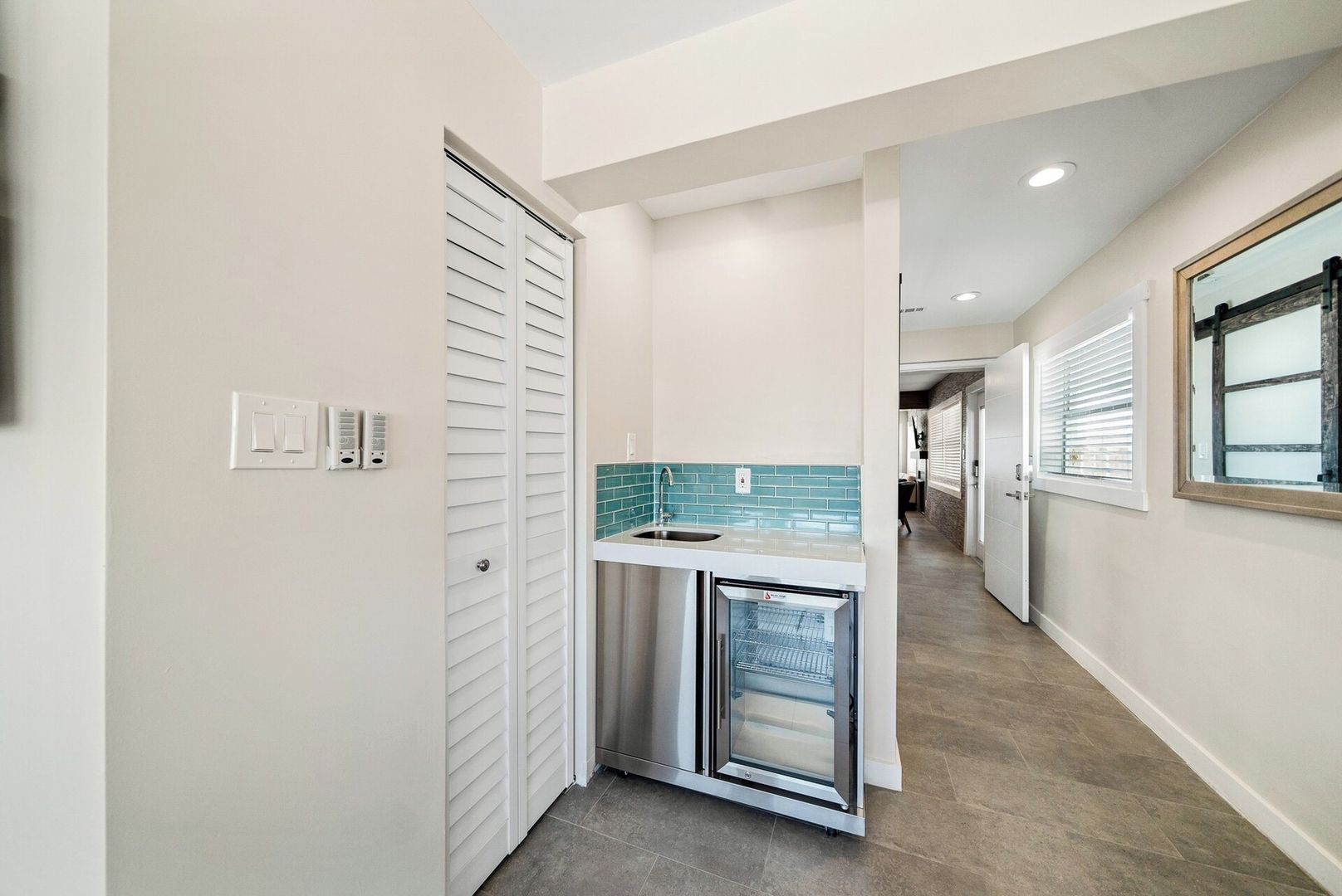 A hallway with a built-in kitchen area featuring a stainless steel refrigerator and a tiled backsplash.
