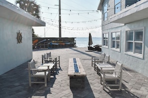 An outdoor patio with wooden benches and a central table, overlooking a body of water. - Compass 2BR Suite - Gourmet Kitchen - Water view (Cocoa Beach)