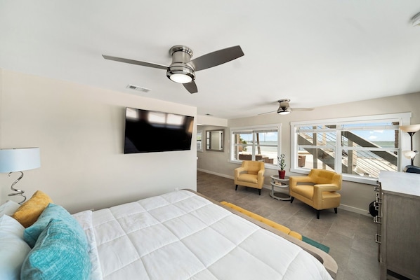A hotel room with a bed, a TV, a ceiling fan, a desk, and a view of the beach. - Compass 2BR Suite - Gourmet Kitchen - Water view (Cocoa Beach)