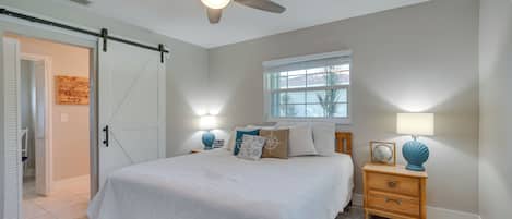 A bedroom with a bed, a nightstand, a lamp, a ceiling fan, a window, and a door.