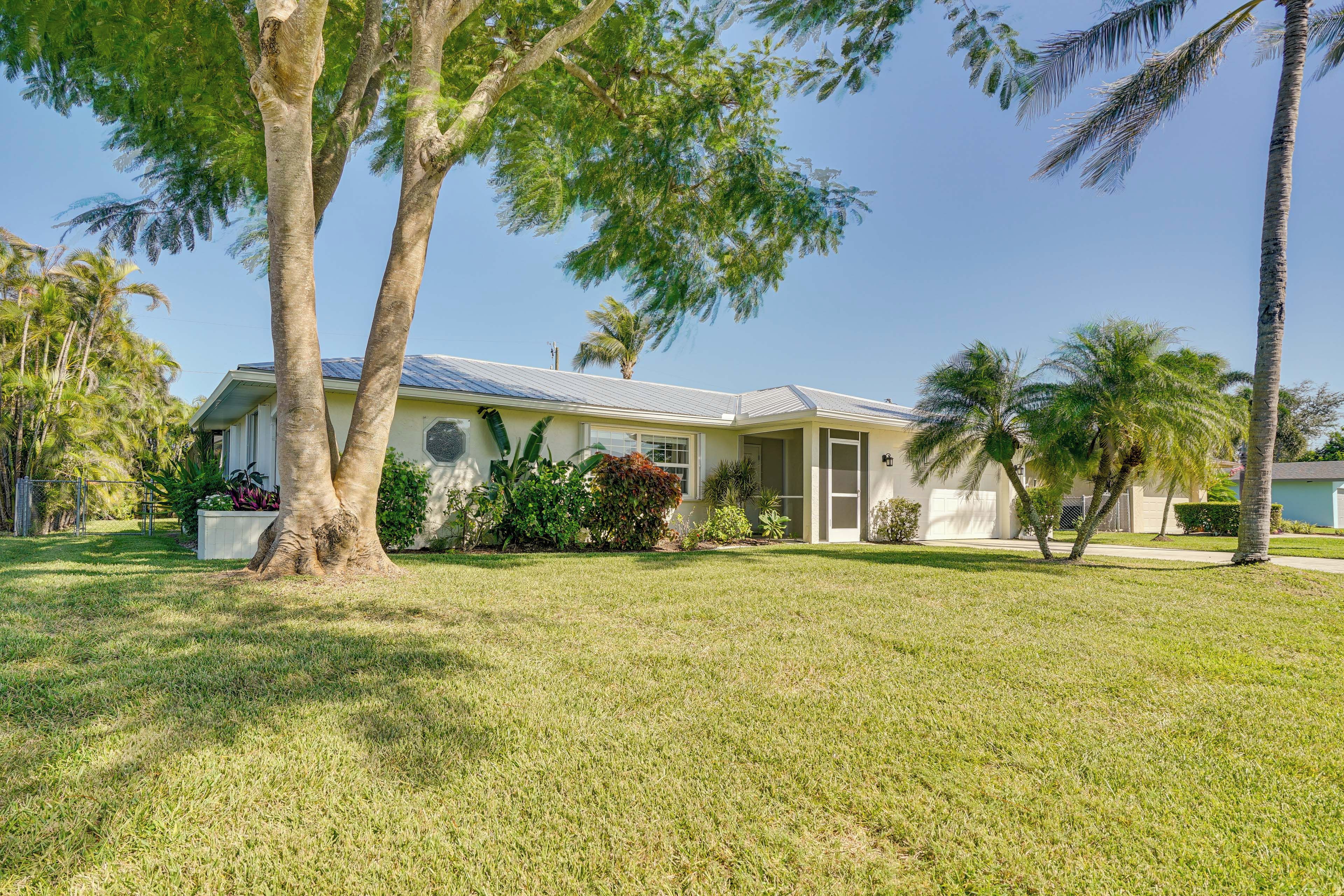 A single-story house with a front lawn, palm trees, and a clear sky.
