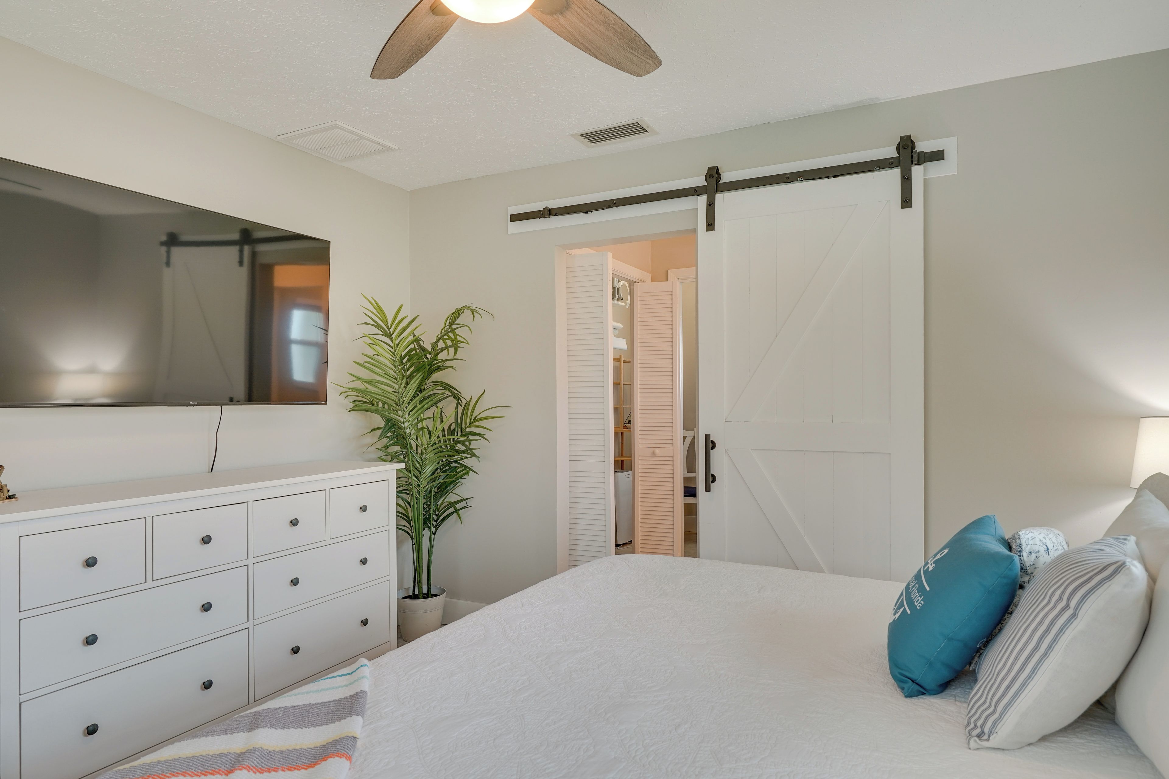 Un dormitorio con cama, cómoda, espejo, puerta corredera y ventilador de techo.