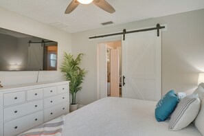 Ein Schlafzimmer mit Bett, Kommode, Spiegel, Schiebetür und Deckenventilator.