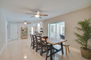 A spacious dining area with a long wooden table and chairs, a ceiling fan, and a large window providing a view of the outdoors.