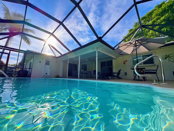 A swimming pool with clear water, surrounded by a covered patio area with chairs and tables.