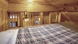 A cozy attic bedroom with wooden walls, a plaid bedspread, and a skylight.