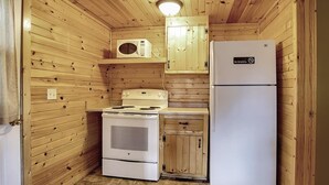 A compact kitchen with a stove, microwave, and refrigerator, wooden walls, and a 'No Smoking' sign.