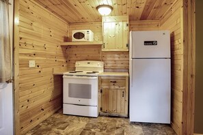 A compact kitchen with a stove, microwave, and refrigerator, wooden walls, and a 'No Smoking' sign. - Cozy River Cabin w/ Loft & Screened Porch (Buffalo City)
