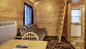 A cabin interior with a sofa, a table with a remote control, a heater, and a window with curtains.