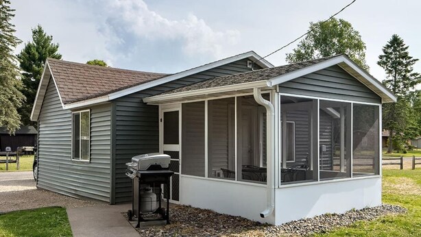 Ein Bungalow mit überdachter Veranda, Grill und Moskitonetz.