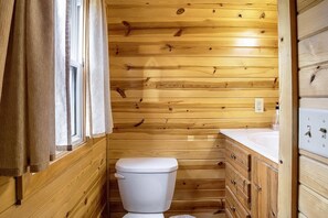 A wooden-paneled bathroom with a toilet, sink, and window.