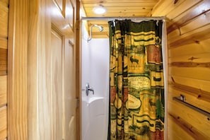 Baño de cabaña de madera con cortina de ducha con estampado de motivos naturales.