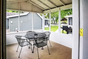 A covered patio with a round table and chairs, large windows, and a view of a backyard.