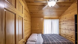 Ein Zimmer mit Holzwänden, einem Bett, einem Deckenventilator und einem Fenster mit Vorhängen.