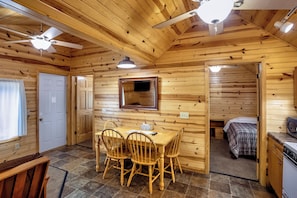 Interior de una cabaña de madera con comedor, cocina y habitación.