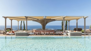 Zona de piscina con área de descanso cubierta, sillas de salón y vista al mar.