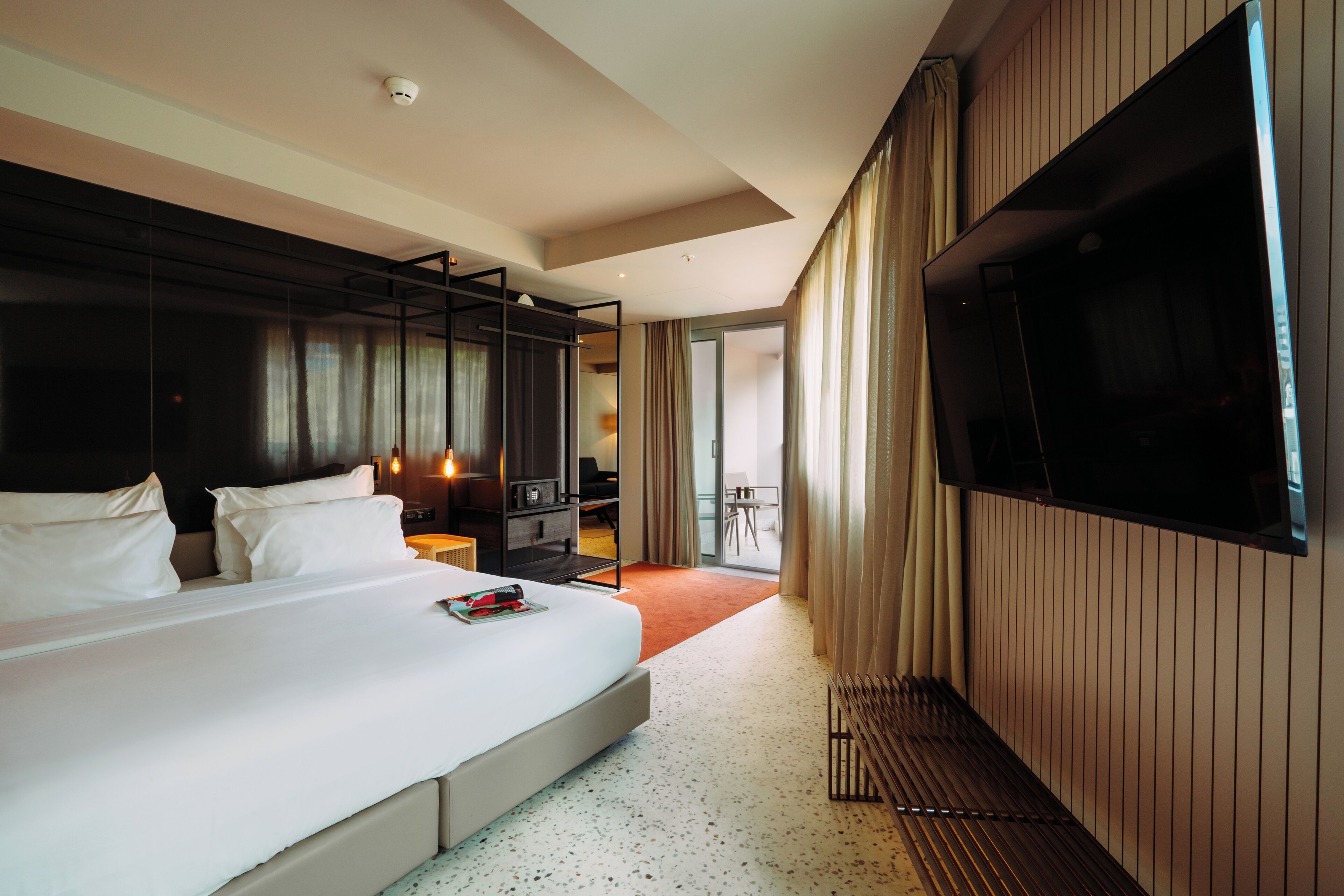 Een moderne hotelkamer met een groot bed, een televisie, een bureau en een balkon met gordijnen.