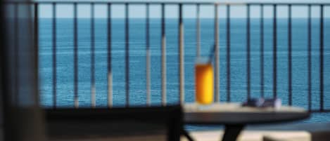 A balcony with a view of the sea, a table with a candle, and a chair.