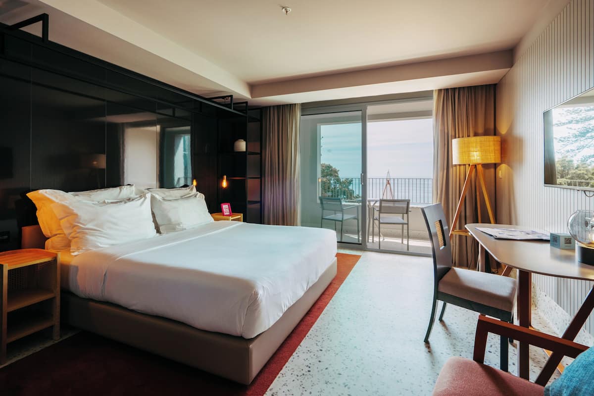 Una habitación de hotel con una cama grande, un escritorio y un balcón con vistas.