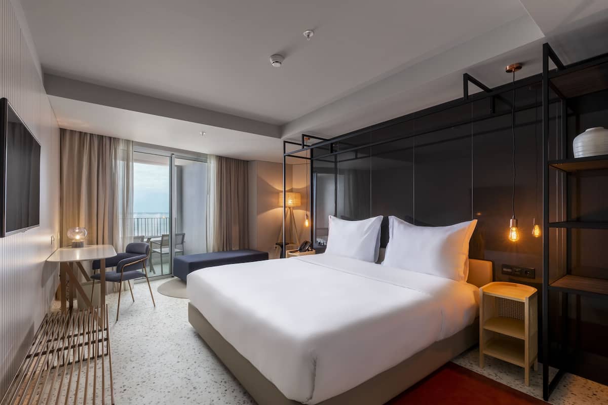 Habitación de hotel moderna con una cama grande, un escritorio, una silla y un balcón con cortinas.
