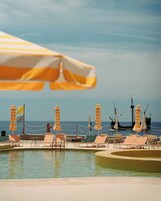 A poolside area with lounge chairs and umbrellas, a checkered flag, and a view of the ocean.