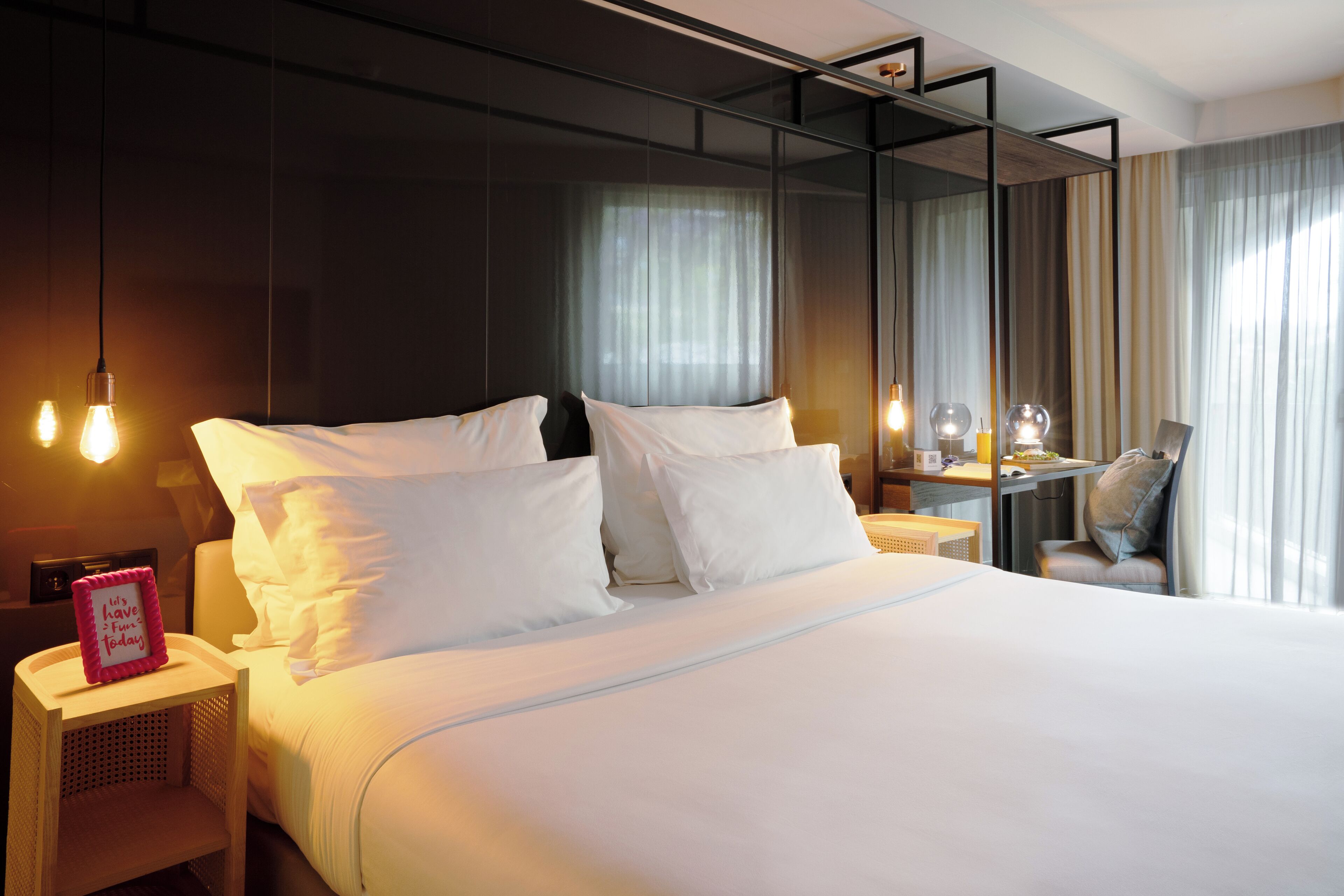 A modern hotel room with a large bed, bedside lamps, a desk, and a chair.