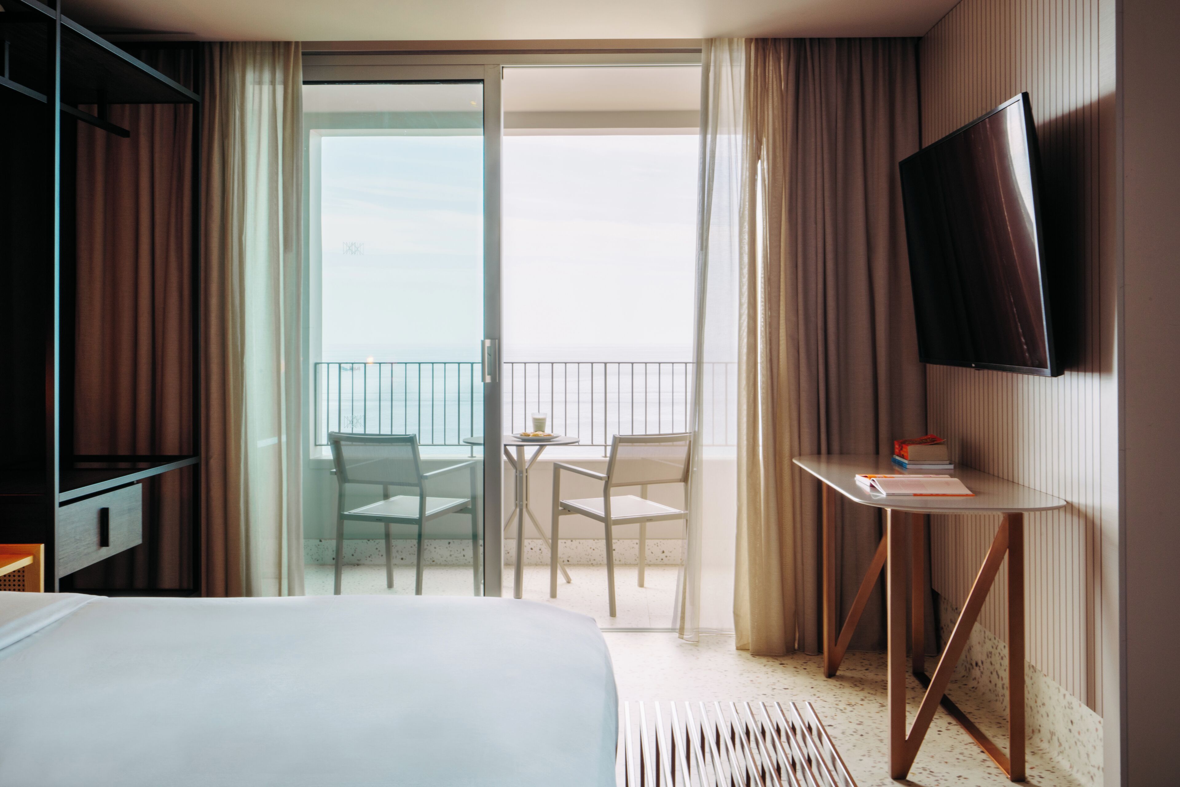 A hotel room with a bed, a desk, a chair, and a TV.